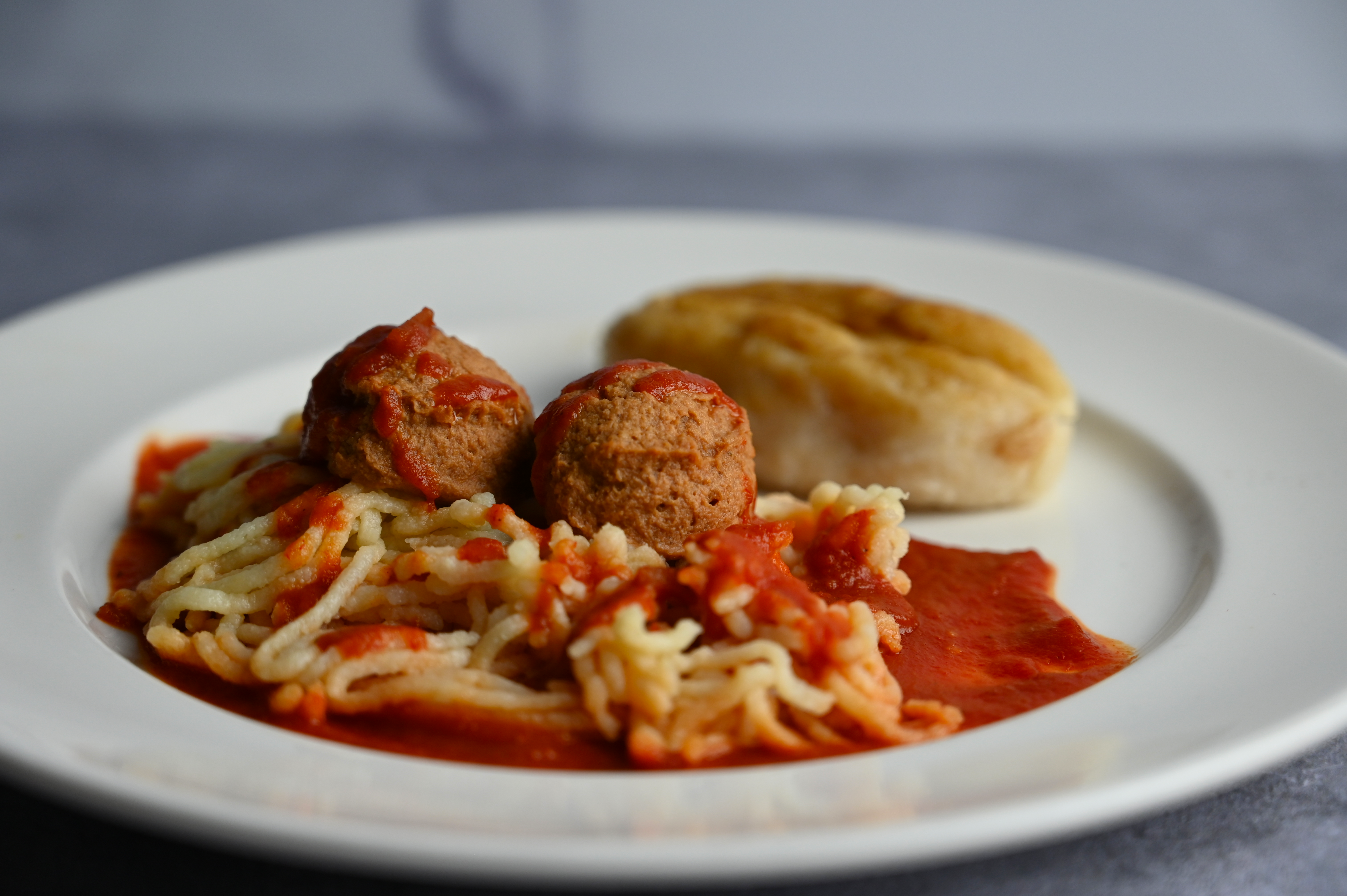 Spaghetti and Meatballs on a plate with red sauce and a bread roll. All of the food is puree
